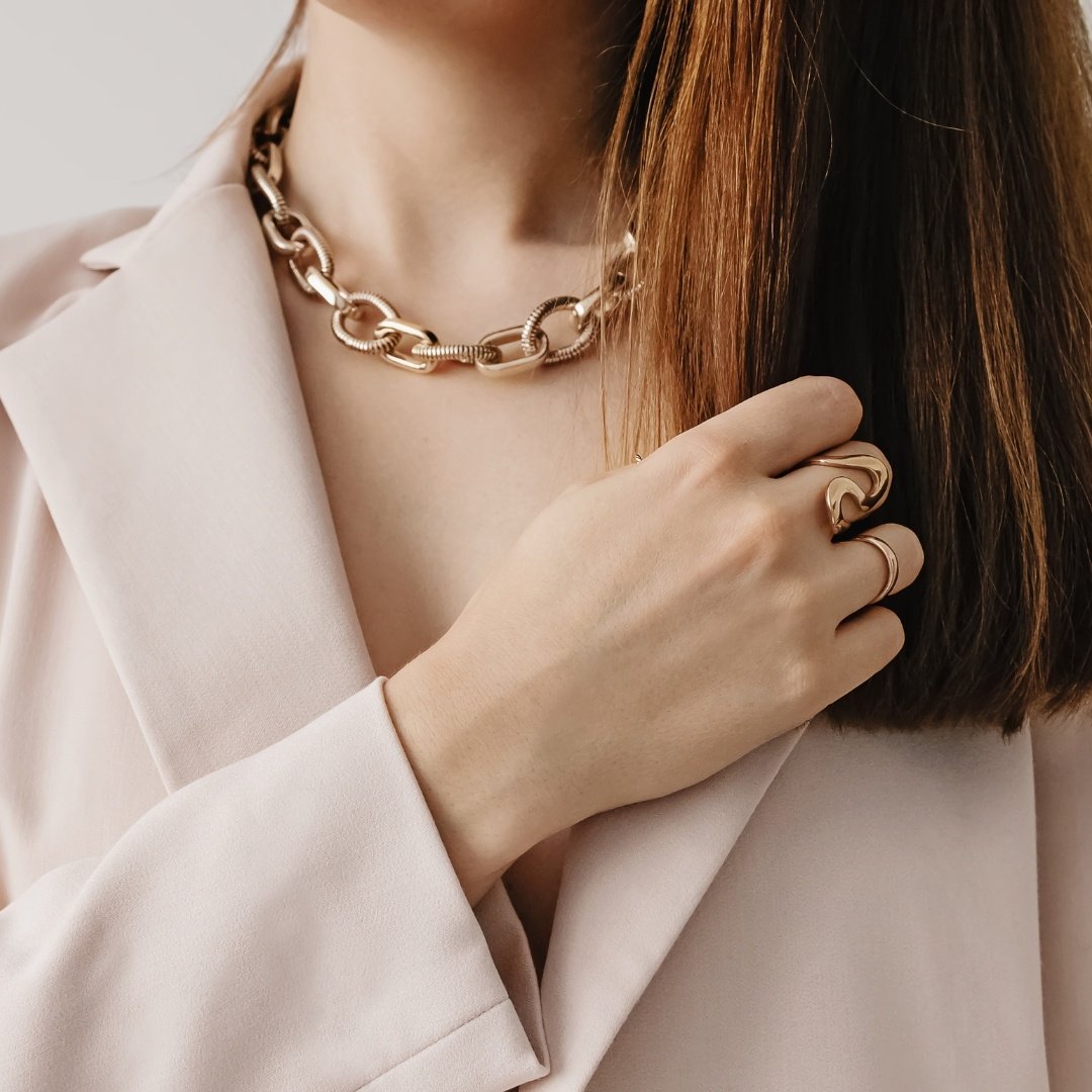 female models hand across her cheat wearing a blazer and gold chain