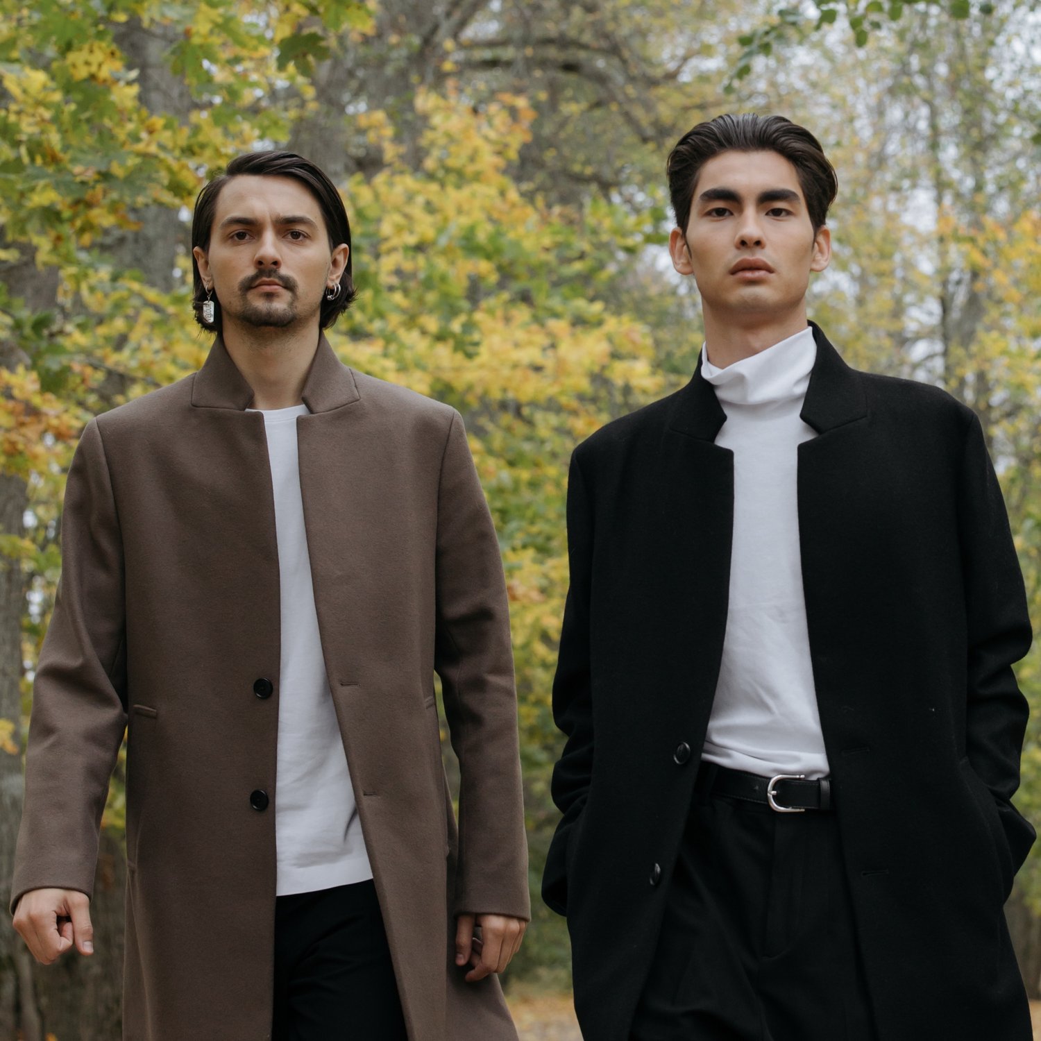 two men in formal wear standing in a forested area