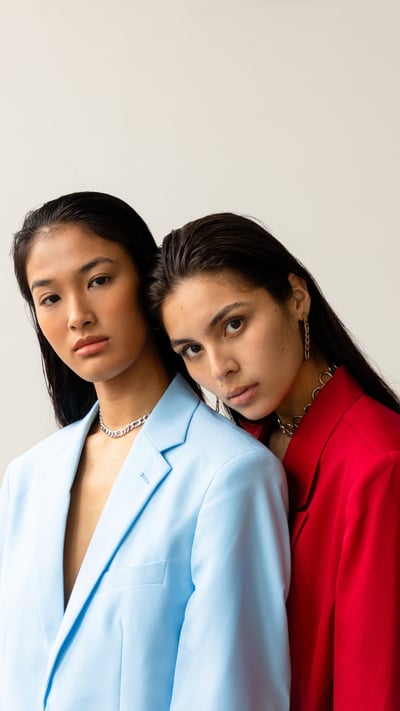 female model in a red suit leaning on a female model in a blue suit with click back hair