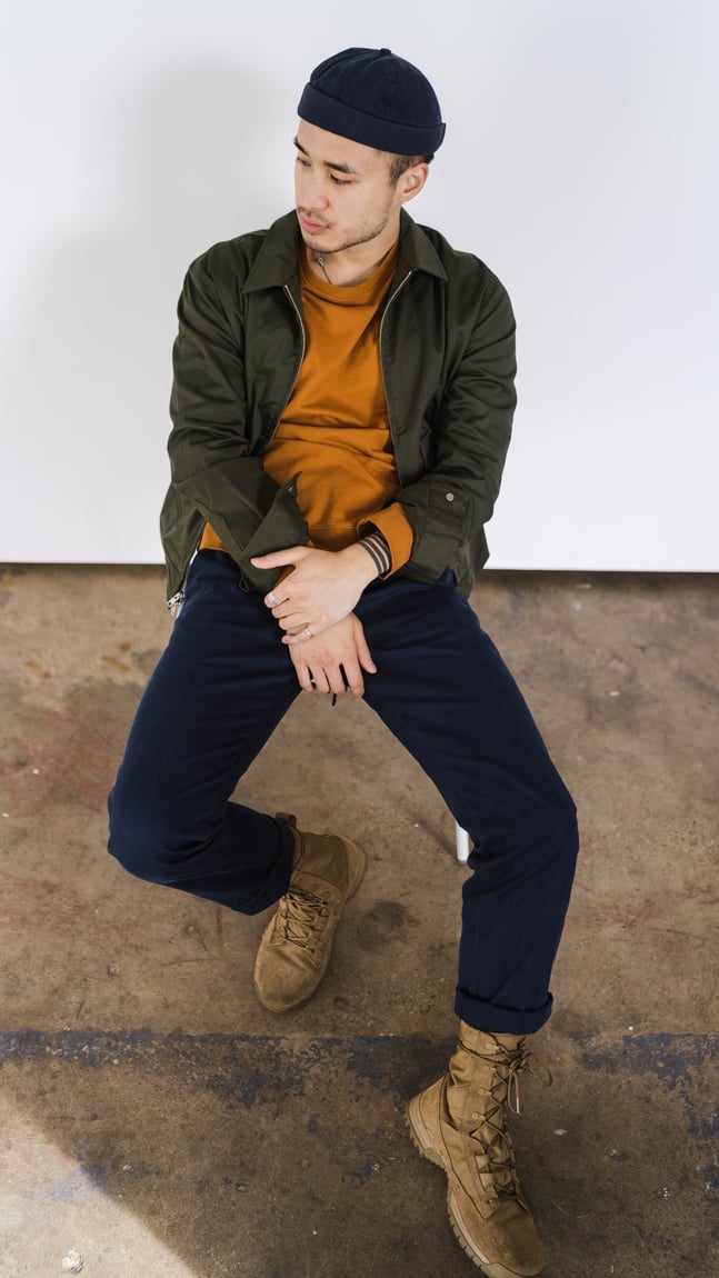 white male model in a mustard shirt with black beanie and chinos sitting in a chair