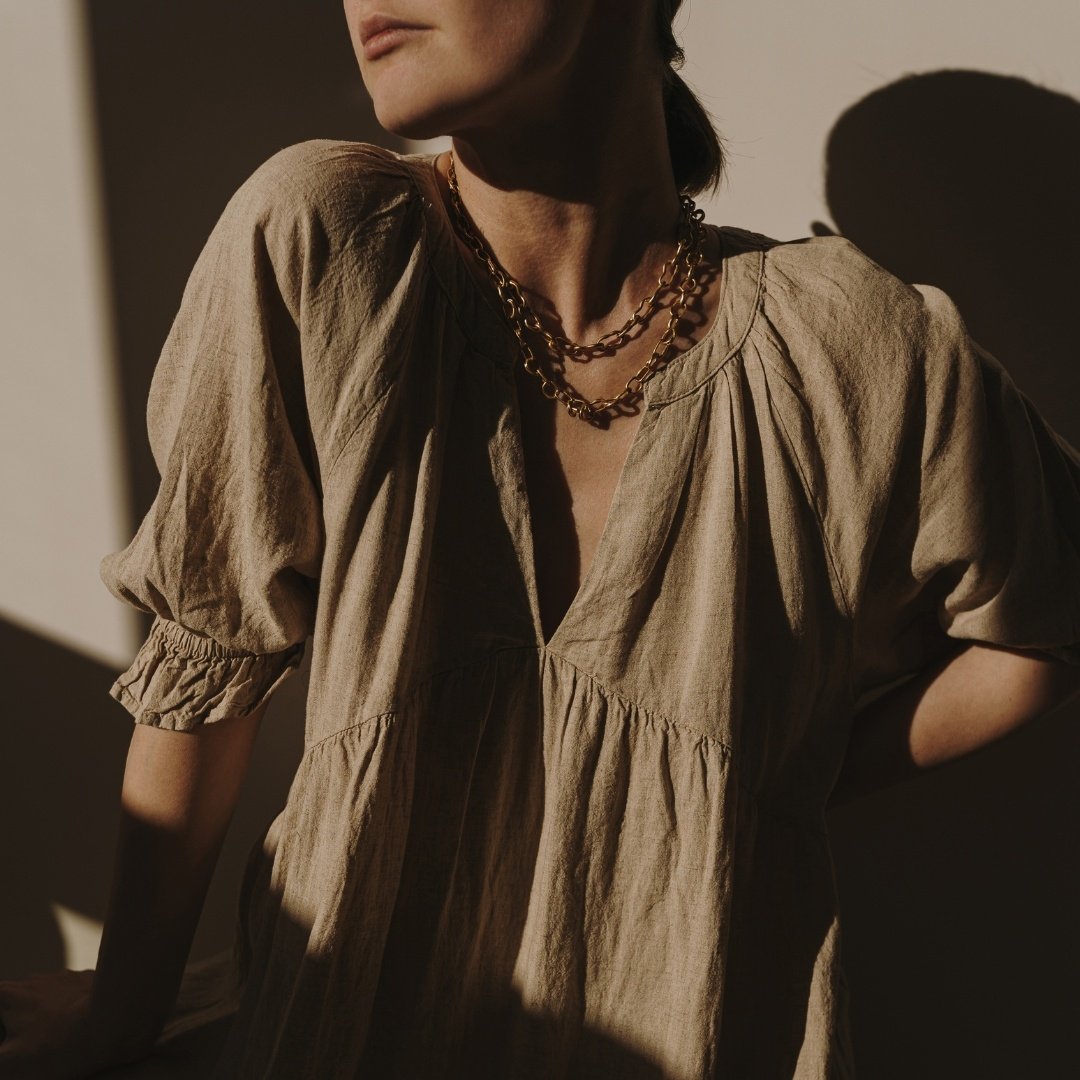 image of a woman from the neck down, in a linen shirt with necklaces