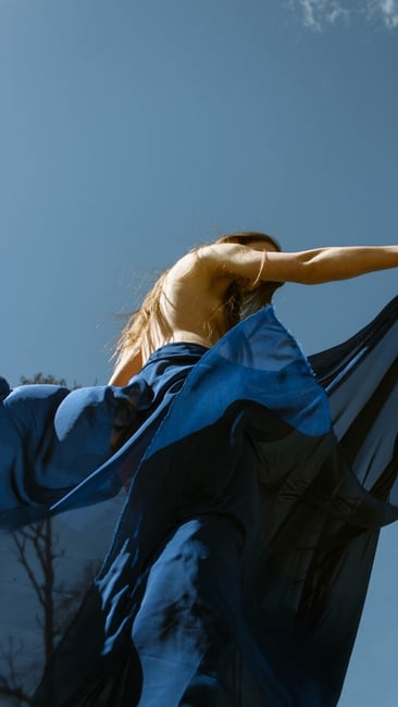 model in blue satin dress with pleats blowing in the wind