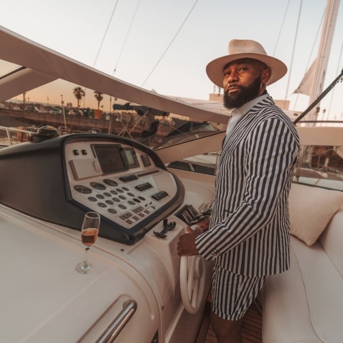 black man in a suit with a hat, driving a yacht