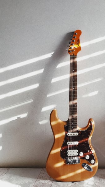 wooden electric guitar leaning against a stone, white wall 