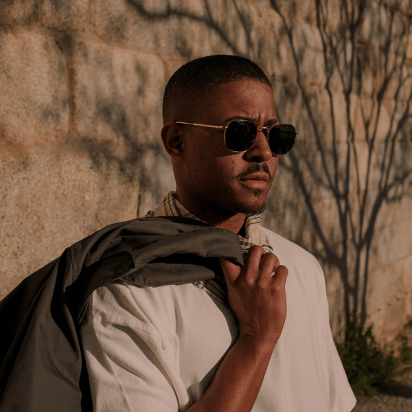 model wearing sunglasses and holding a blazer over his shoulder