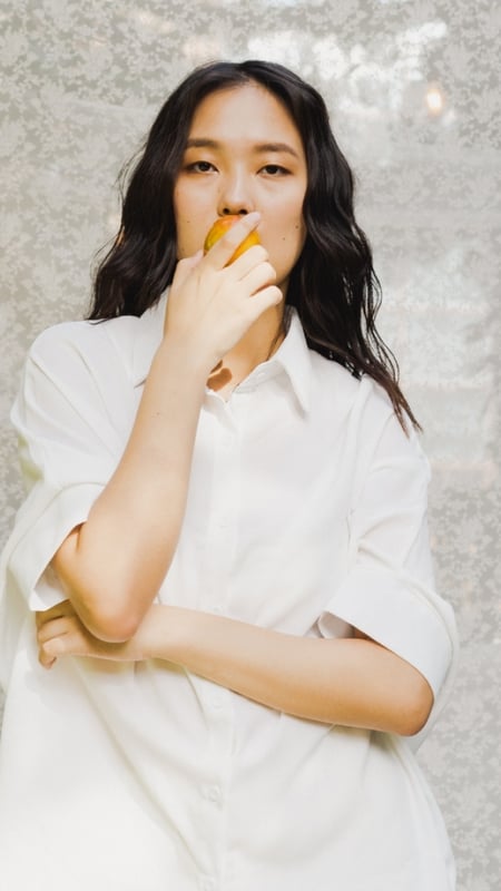 asian woman with long hair, biting on an apple, staring into the camera