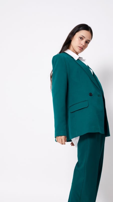 woman in a turquoise suit with back bent, body angled away from the camera and face turned to the lens