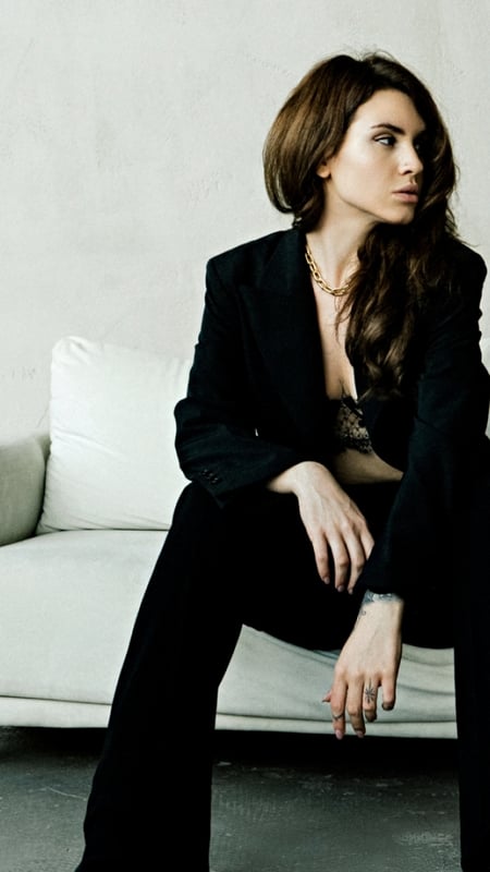 woman in black suit sitting on a white sofa, looking away from the camera