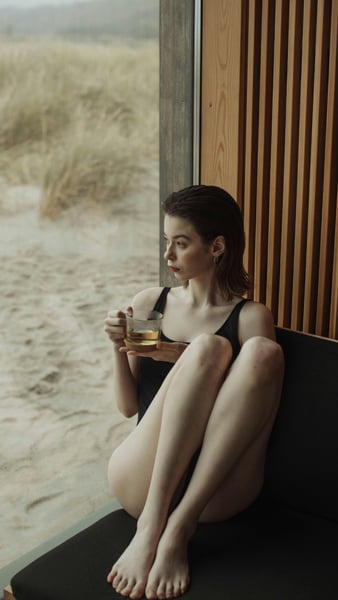 woman staring out the window in a black t shirt, holding a cup of tea