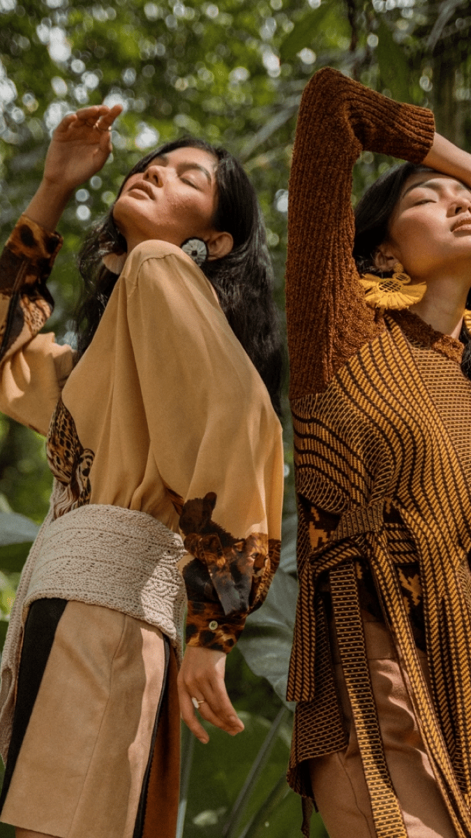  Two women wearing brown and yellow outfits stand in a lush forest, creating a harmonious connection with nature
