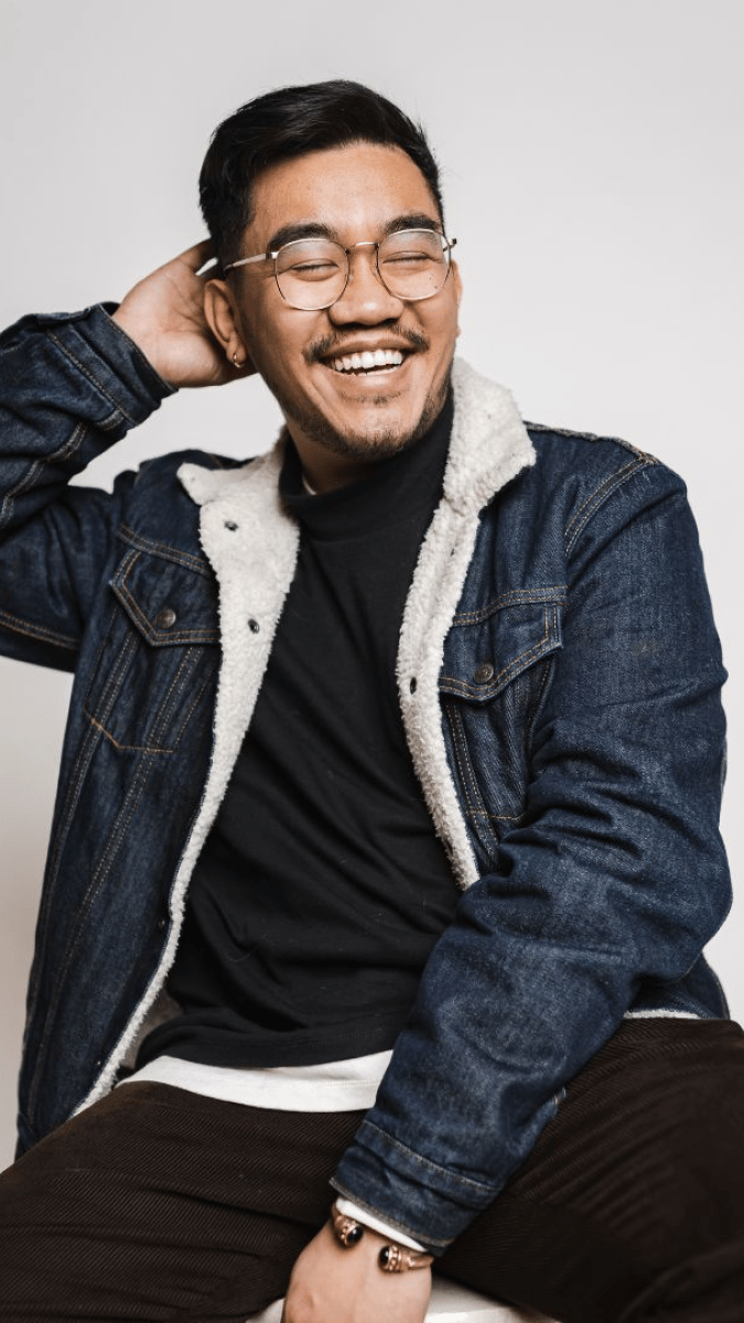 young guy in wool denim jacket, sitting down with eyes closed, laughing