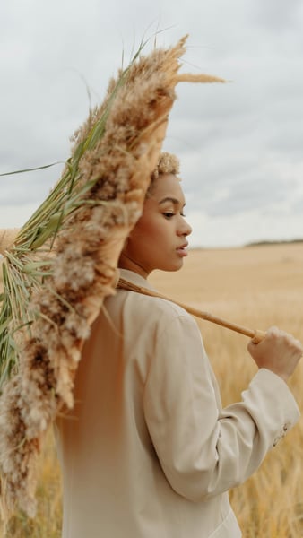 woman holding a flower umbrella, standing in grass fields, looking away from the camera 