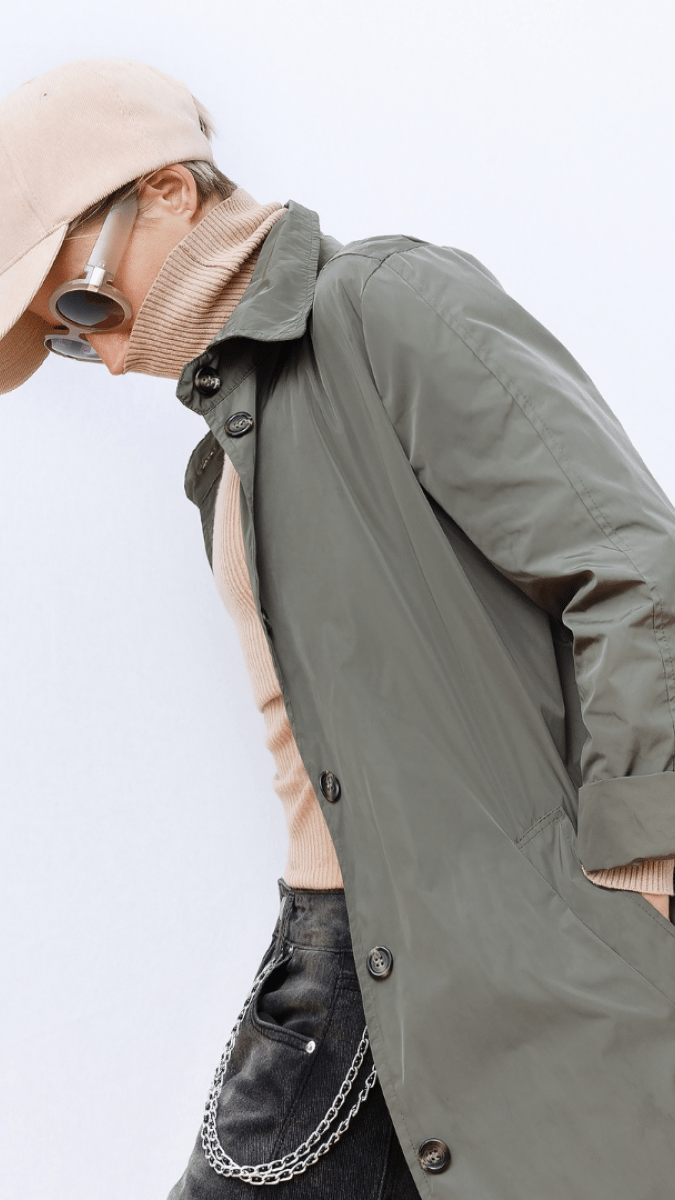 woman in a sunglasses, khaki raincoat, turtle neck and peach cap walking by the camera 