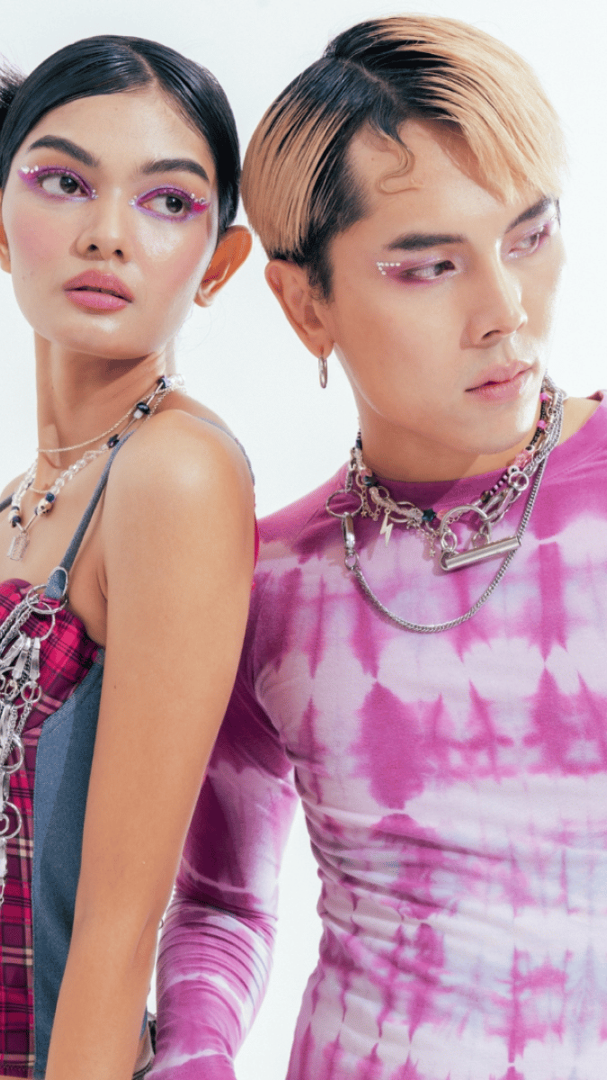 Male and female model wearing pink tones with silver jewellery and pink eye shadow, both looking away from the camera