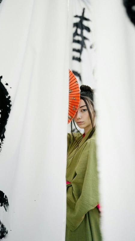 asian woman in a kimono, holding an orange fan, half visible behind a white sheet