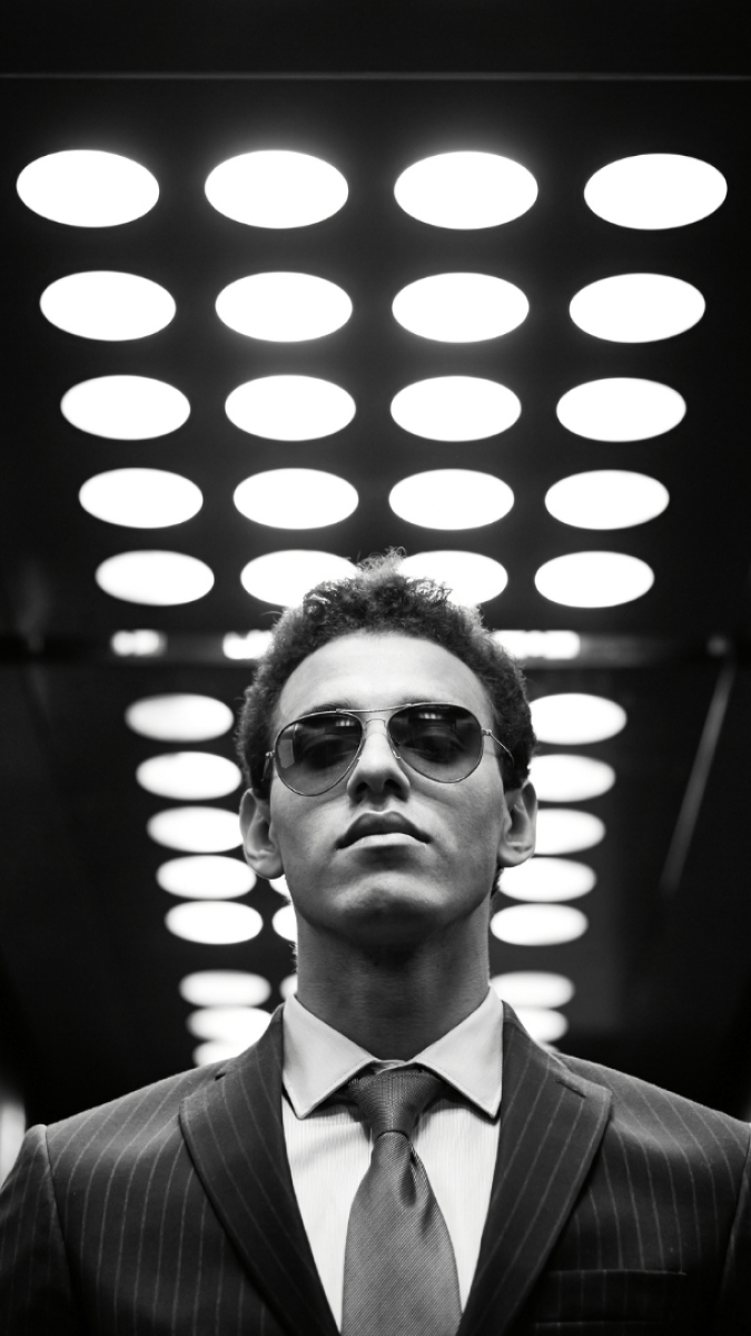 young man wearing a suit and tie, photographed in black and white from the chest up, wearing sunglasses