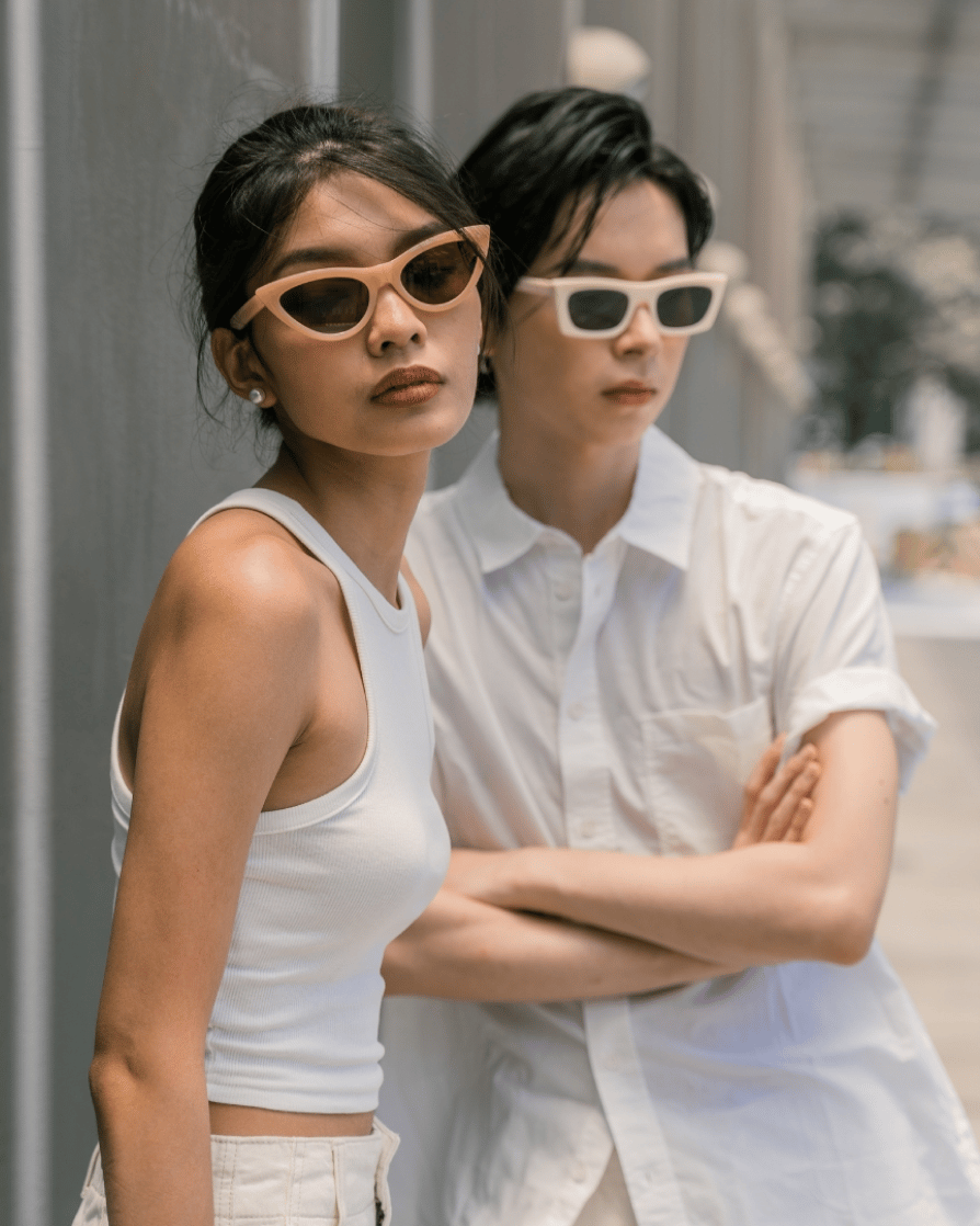 two woman standing against a wall, wearing white outfits paired with sunglasses 