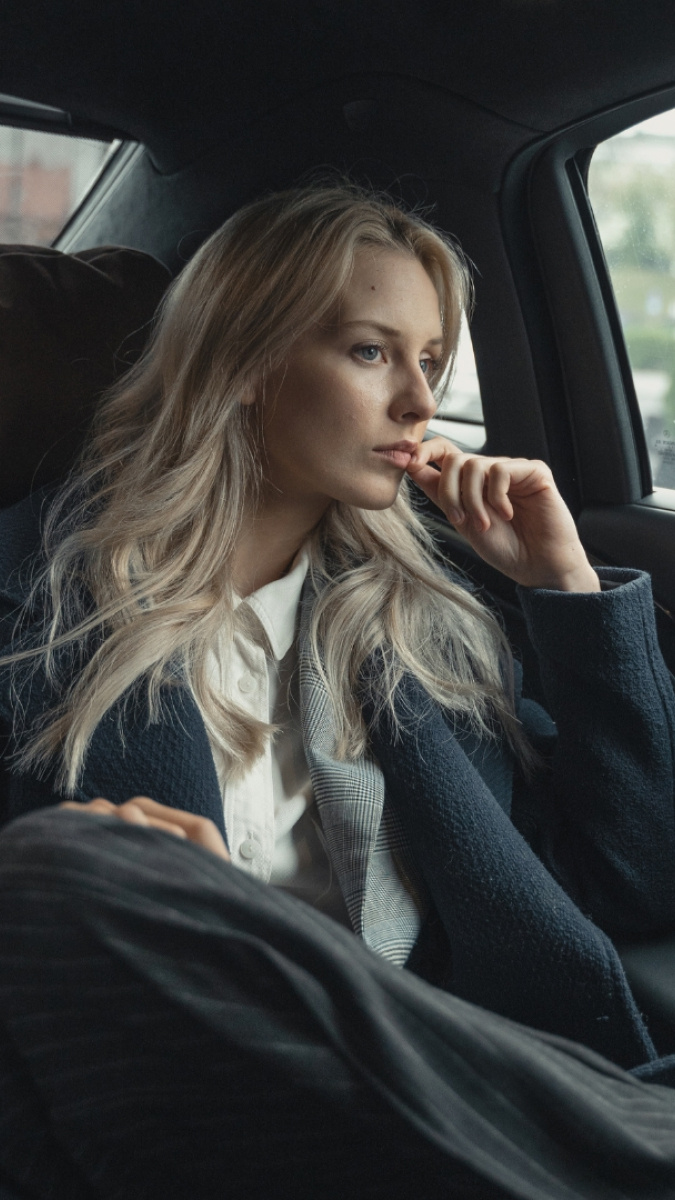 Blonde woman in business suit and a white dress shirt, staring out the car window with a serious face