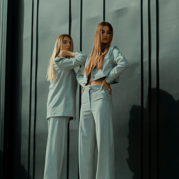 Two women with long blonde hair, dressed in light blue formal attire and looking into the distance