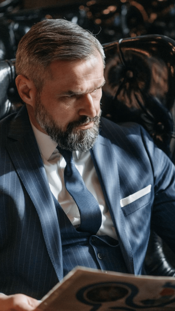 man in a blue suit with slick back grey hair, reading