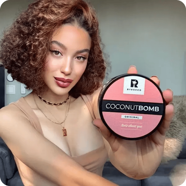 An influencer with short, curly reddish hair holding up Byrokko's Coconut bomb