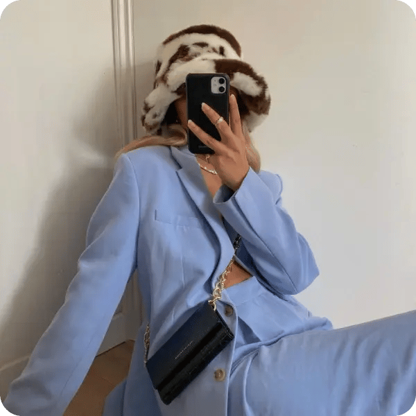 A model in a baby blue suit wearing a fluffy hat and a black Ideal of Sweden bag