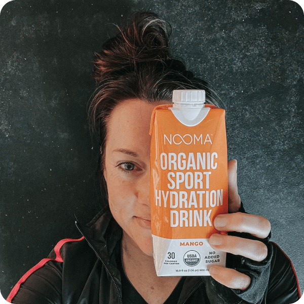 A woman showing half of her face, with the other half covered by Nooma's organic sport hydration drink