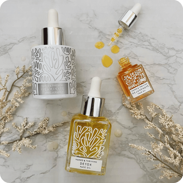 Naked &amp; Thriving products laid out on a granite countertop with flowers scattered around the product