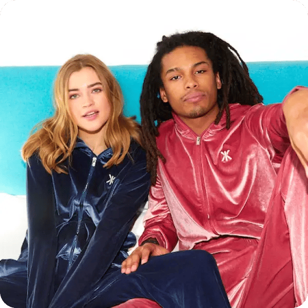 A woman with blonde hair in a navy Onepiece outift and a man with brown dreadlocks wearing a pink Onepiece suit