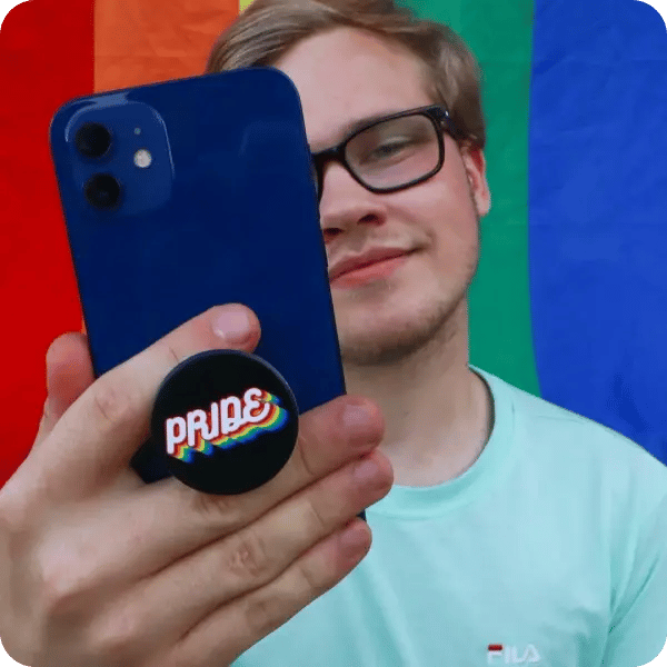 A male influencer with blonde hair holding up a blue phone case with a "PRIDE" popsocket