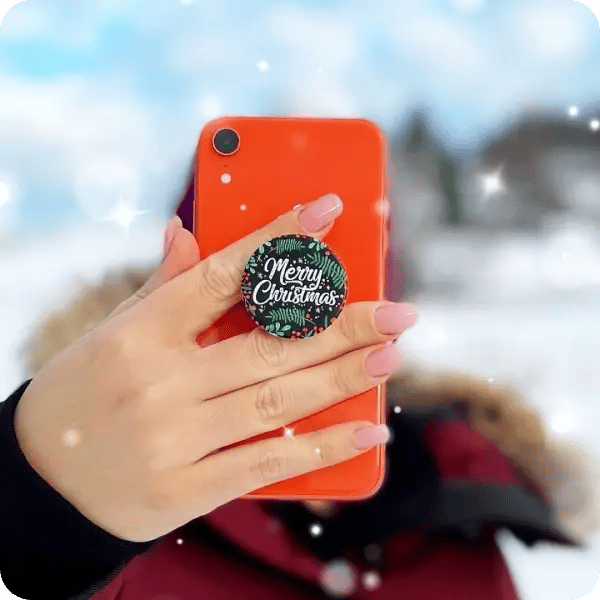 Person wearing a puffer jacket, holder her phone up with a red phone case and a Merry Christmas phone case