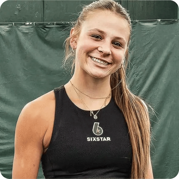 A woman in a black Sixstar sports vest standing on a tennis court, smiling at the camera